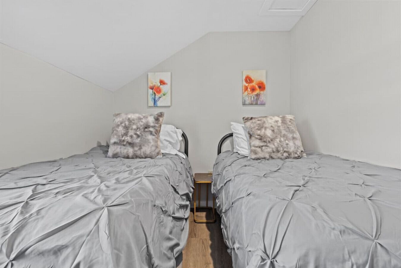 A twin bedroom with two beds, each with grey bedding and decorative pillows. There are two paintings on the wall above the beds.