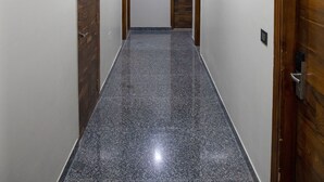 A hallway with a polished granite floor, white walls, and wooden doors. - Dev Royale Hotel (Gurugram)
