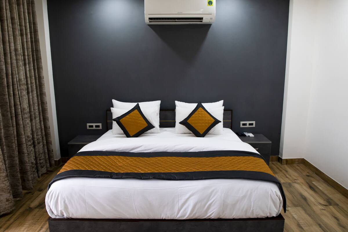 A modern hotel room with a large bed, dark walls, and a wooden floor.