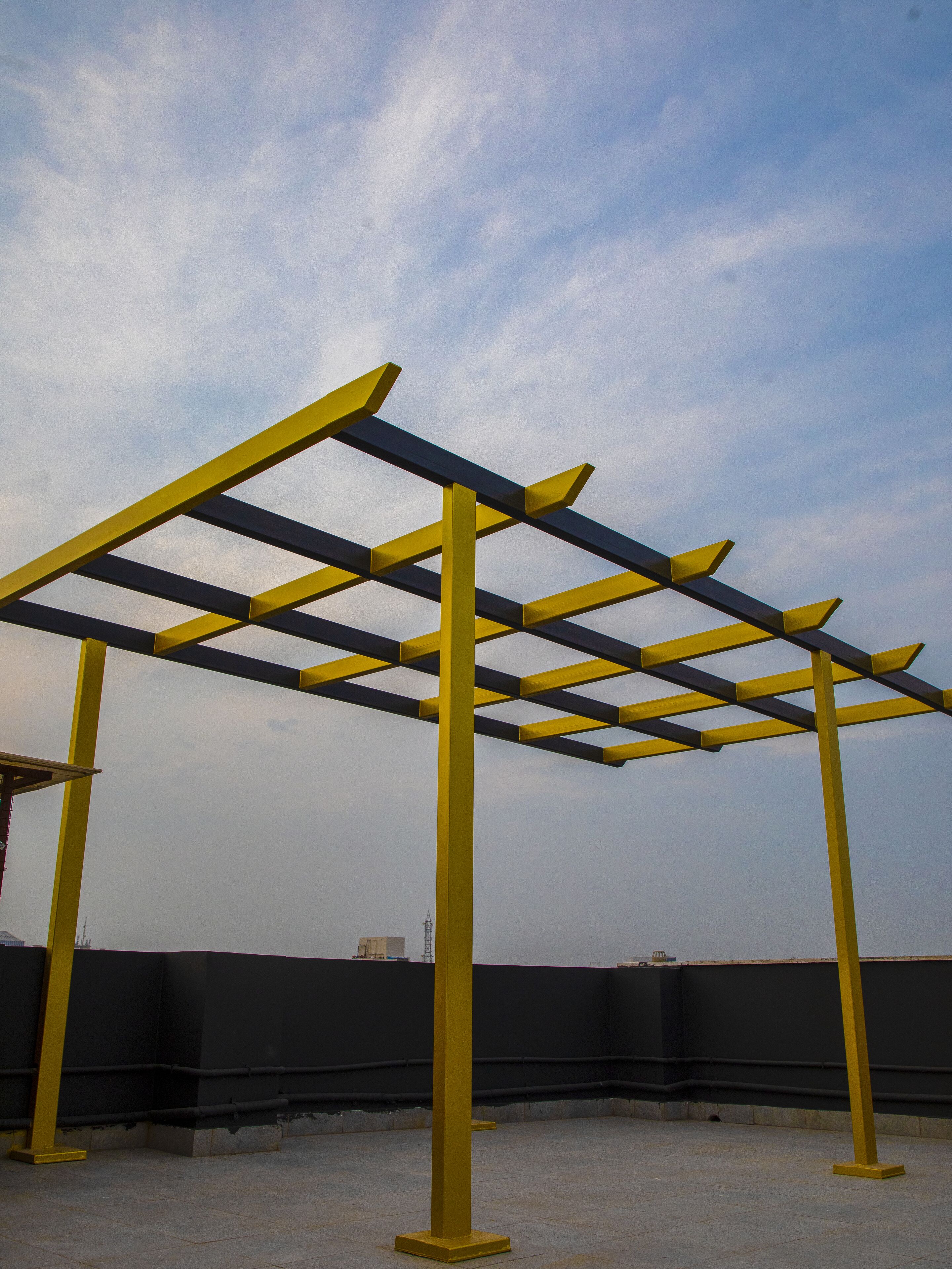 En guldfärgad metallkonstruktion med ett rutmönster, troligen en pergola, på ett hustak med en klar himmel i bakgrunden.