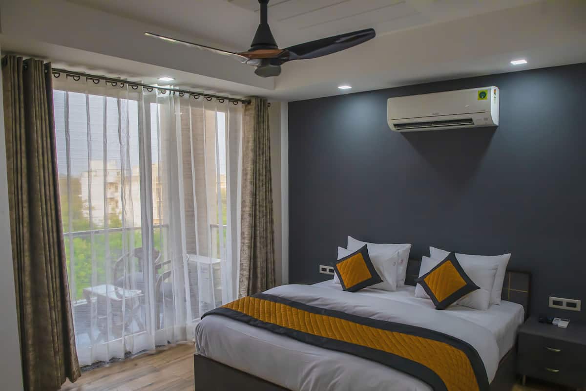 A bedroom with a bed, a ceiling fan, an air conditioning unit, and a view through a window with curtains.