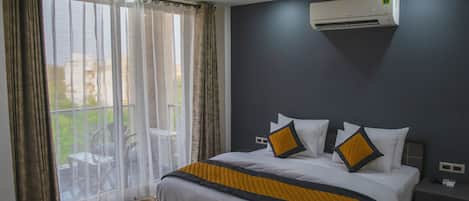 A bedroom with a bed, a ceiling fan, an air conditioning unit, and a view through a window with curtains.