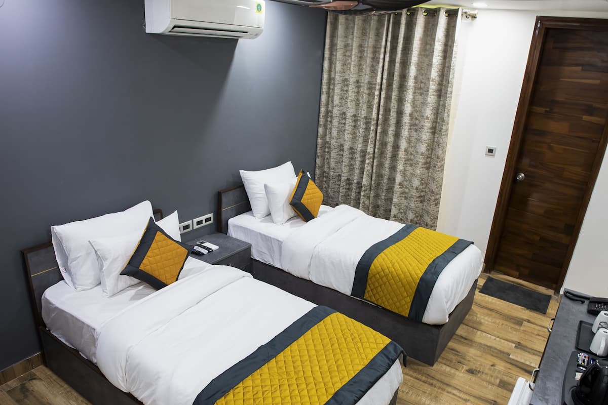 A hotel room with two beds, a desk, a coffee machine, and a door.