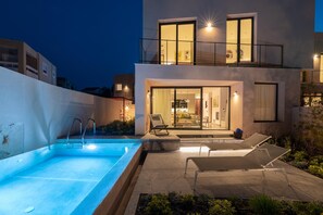 Una casa moderna de dos pisos con piscina, mobiliario exterior y un balcón.