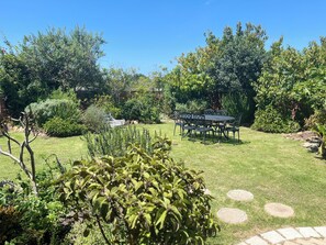 A well-maintained garden with a dining area featuring a table and chairs, surrounded by various plants and trees.