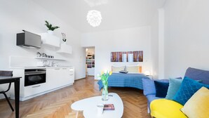 A modern living room with a sofa, coffee table, and a kitchen area with white cabinets and a built-in oven. - Beautiful Mala Strana Studio by EasyBNB Premium (Prague)