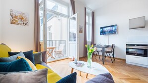 A modern living room with a sofa, coffee table, and a dining area with chairs. There is a TV mounted on the wall and a window with curtains. - Beautiful Mala Strana Studio by EasyBNB Premium (Prague)