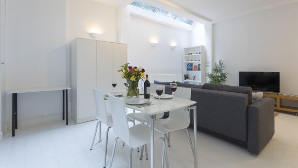 A modern living room with a dining area, white furniture, a grey sofa, a TV, and a bookshelf. - Large flat near Oxford Circus (London)