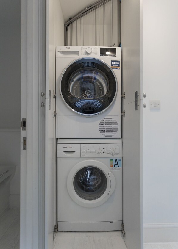 A compact, white stacked washer and dryer unit in a narrow hallway. - Large flat near Oxford Circus (London)
