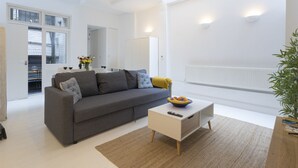 A modern living room with a grey sofa, a white coffee table, and a large window. - Large flat near Oxford Circus (London)