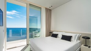 A modern hotel room with a large bed, a nightstand with a lamp, and a view of the ocean through a sliding glass door. - Luxury sea front villa with pool, Lido di Noto, Sicily (Noto)