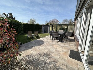 A patio area with a table and chairs, a small garden, and a shed. - 5-personen-ferienhaus in Ruhigem Park (Brouwershaven)