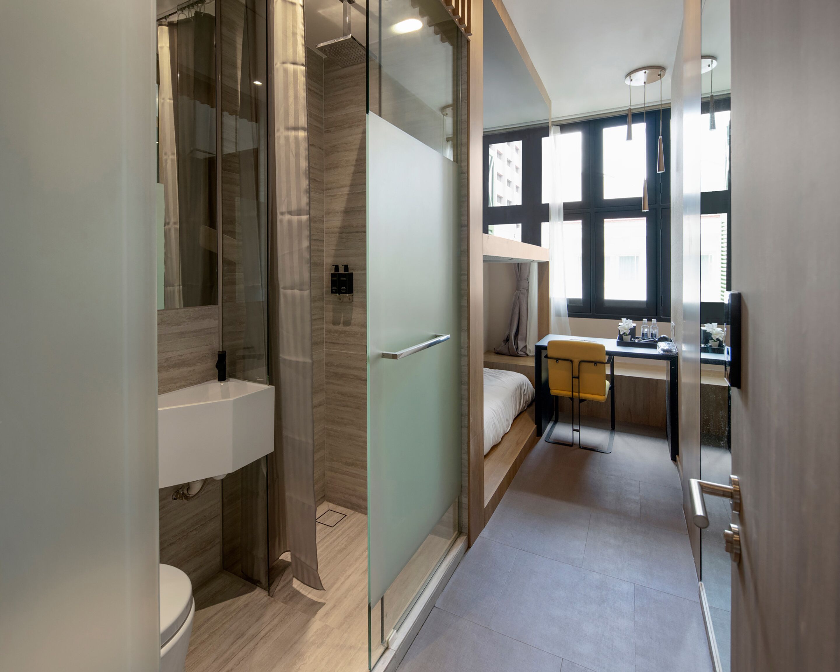 Habitació d'hotel petita amb dutxa, vàter, llit i una petita taula amb una cadira.
