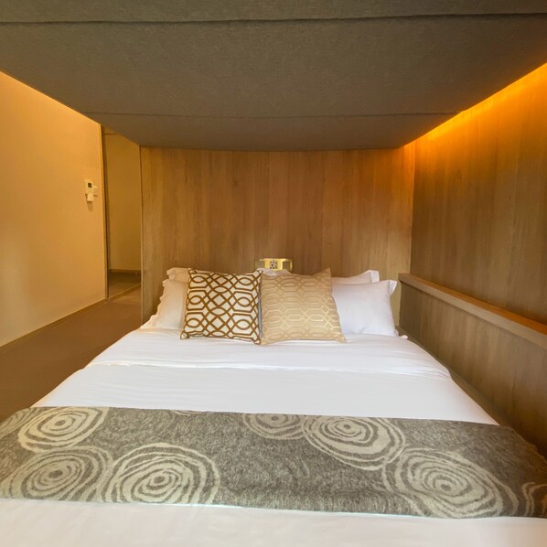A hotel room with a bed, pillows, and a headboard.