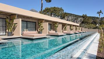 Un hotel moderno con una piscina larga, asientos al aire libre y montañas al fondo.
