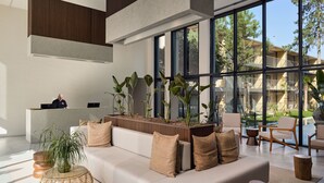 A modern hotel lobby with a reception desk, a white sofa with beige cushions, and large windows offering a view of the outdoors. - Balmy Beach Resort Kemer (Kemer)