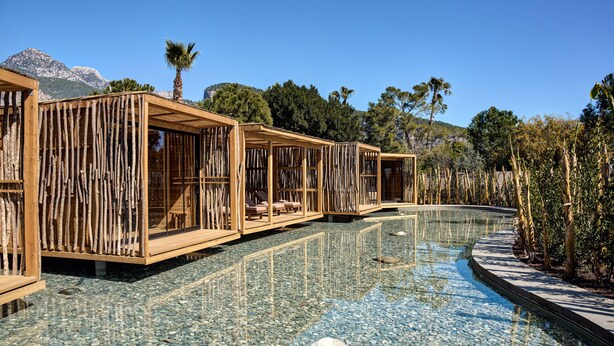 A pool area with wooden structures, clear water, and a pebble ground. - Balmy Beach Resort Kemer (Kemer)