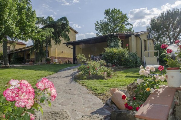 Ein Gartenweg führt zu einem Gebäude mit einem Ziegeldach und einer überdachten Terrasse.