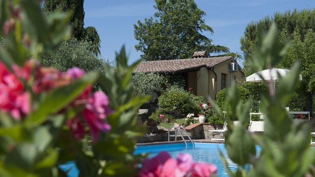 A pool area with a clear view of the pool, a chair, and a building with a tiled roof. - Allodola double bedroom flat facing pool with large veranda (Toscana)