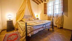 A bedroom with a four-poster bed, a nightstand with a lamp, a red patterned rug, and a wooden ceiling. - Allodola double bedroom flat facing pool with large veranda (Toscana)