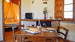 A dining area with a wooden table, chairs, a fireplace, and a bed with a canopy. - Allodola double bedroom flat facing pool with large veranda (Toscana)