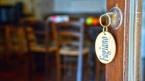 Una puerta de madera con un ojo de cerradura y una placa de madera redonda donde está grabado el nombre "Fugino".