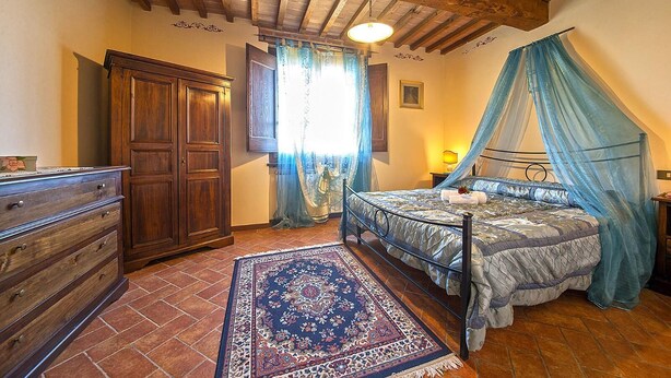 Un dormitorio con cama, mesita de noche, cómoda, ventana con cortinas y techo de madera.