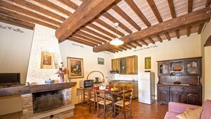 Una cocina acogedora con vigas de madera, chimenea y zona de comedor con un sofá rosa.