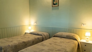 Ein Zimmer mit zwei Einzelbetten, jeweils mit Nachttisch und Lampe, sowie einem kleinen Bild an der Wand.