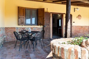 Un patio exterior con una mesa, sillas, una puerta de madera y un muro de ladrillo.