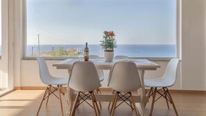 A dining area with a table and chairs facing a large window overlooking the sea. - Steliana's House Top Floor Apartment with Private Jacuzzi (Ligaria)