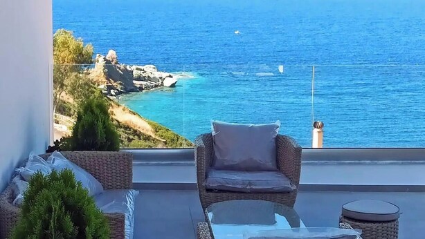 A balcony with wicker furniture, a view of the sea, and a rocky coastline. - Steliana's House Top Floor Apartment with Private Jacuzzi (Ligaria)