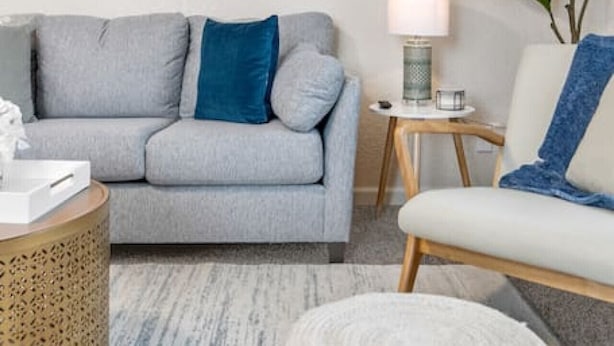 A modern living room with a grey sofa, a white armchair, a round coffee table, and a side table with a lamp. - Beautiful & Convenient! (Sheboygan)