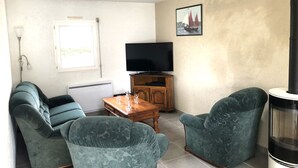 Een woonkamer met een bank, twee fauteuils, een houten salontafel, een televisie en een open haard.