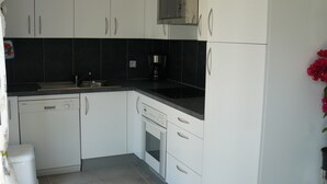 Een moderne keuken met witte kastjes, een magnetron, een koffiezetapparaat en een vaatwasser.