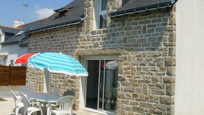 Een stenen huis met een patio tafel en stoelen, een gestreepte parasol, en een houten hek op de achtergrond.