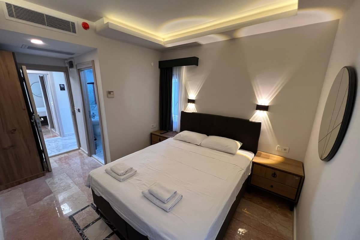 Habitación de hotel moderna con una cama grande, dos mesitas de noche, un espejo y una puerta que da al baño.