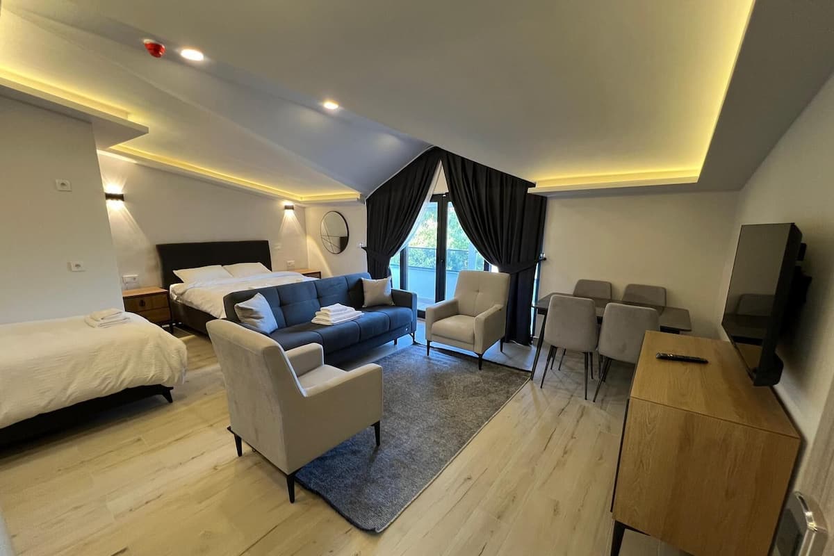 Una habitación de hotel moderna con cama, sofá, sillón, escritorio y televisión.