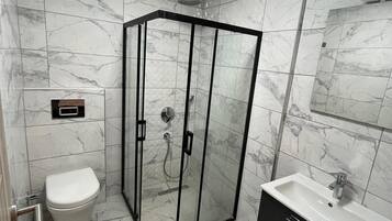 Un baño moderno con ducha envuelta en vidrio, inodoro blanco y tocador negro con lavamanos.