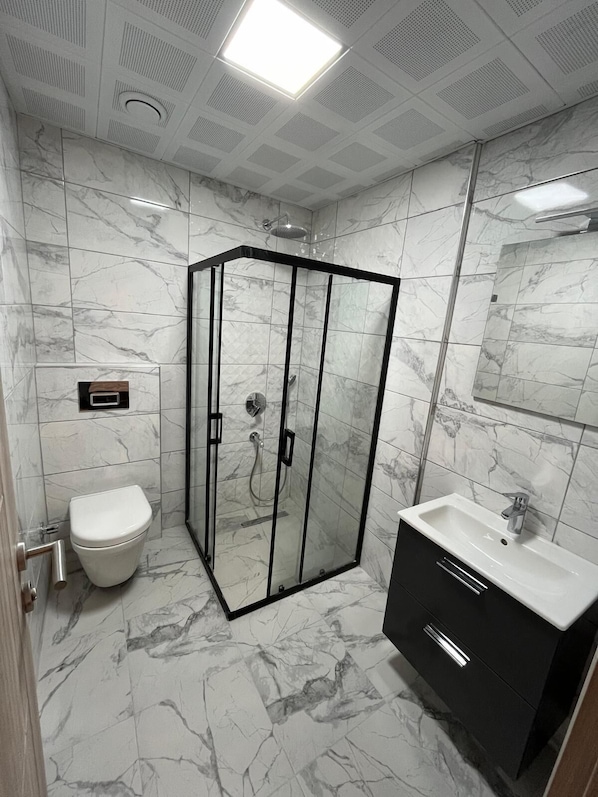 Un baño moderno con ducha envuelta en vidrio, inodoro blanco y tocador negro con lavamanos.