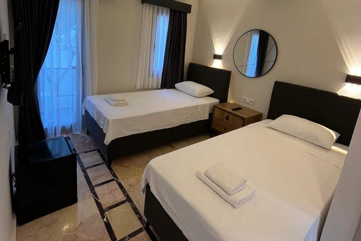 Habitación de hotel con dos camas, una mesita de noche, un espejo y una ventana con cortinas.