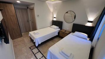 Una habitación de hotel con dos camas individuales, un armario de madera, un espejo redondo y una mesita de noche pequeña con una lámpara.