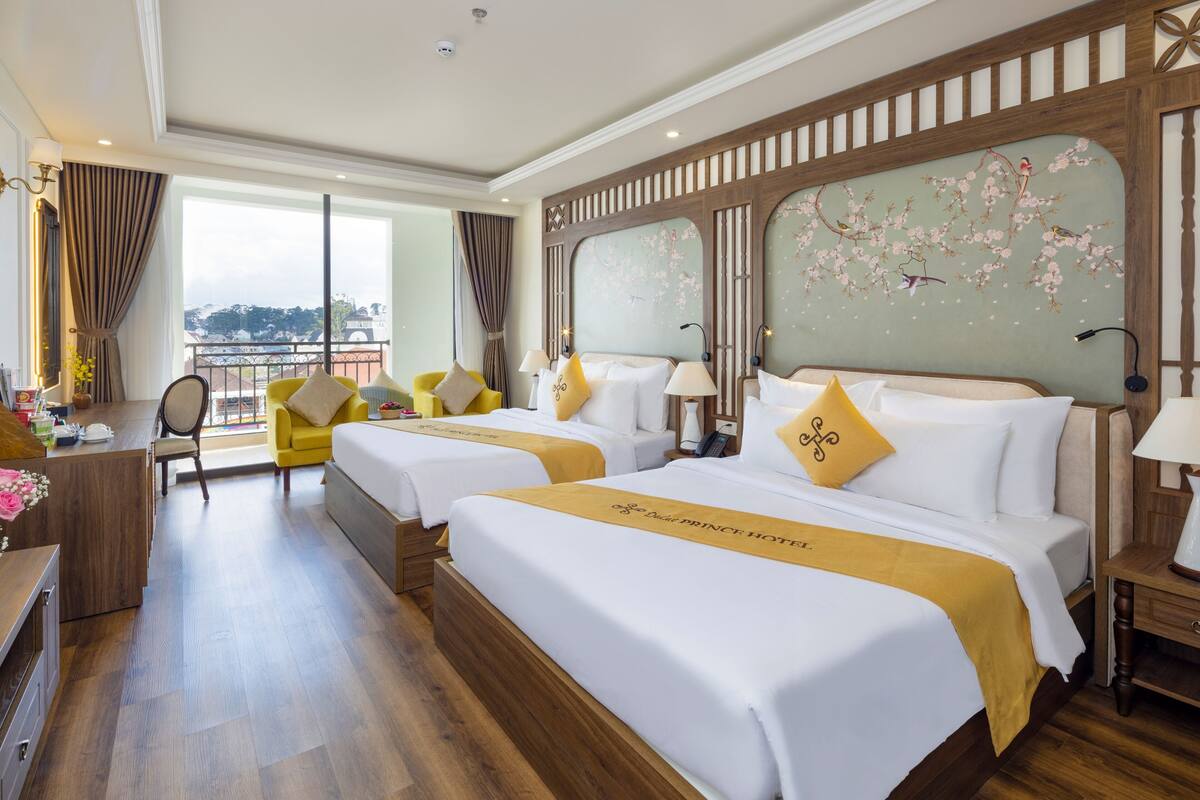 Ein Hotelzimmer mit zwei Betten, einem Schreibtisch, einem Stuhl und Blick auf die Stadt.