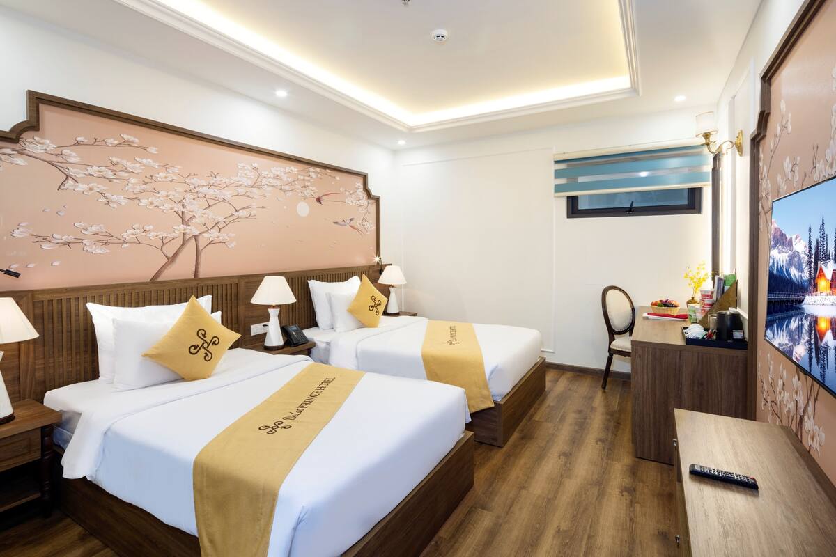 Ein Hotelzimmer mit zwei Betten, Holzboden, einer großen Blumenmalerei, einem Fernseher und einem Schreibtisch mit Fernbedienung.