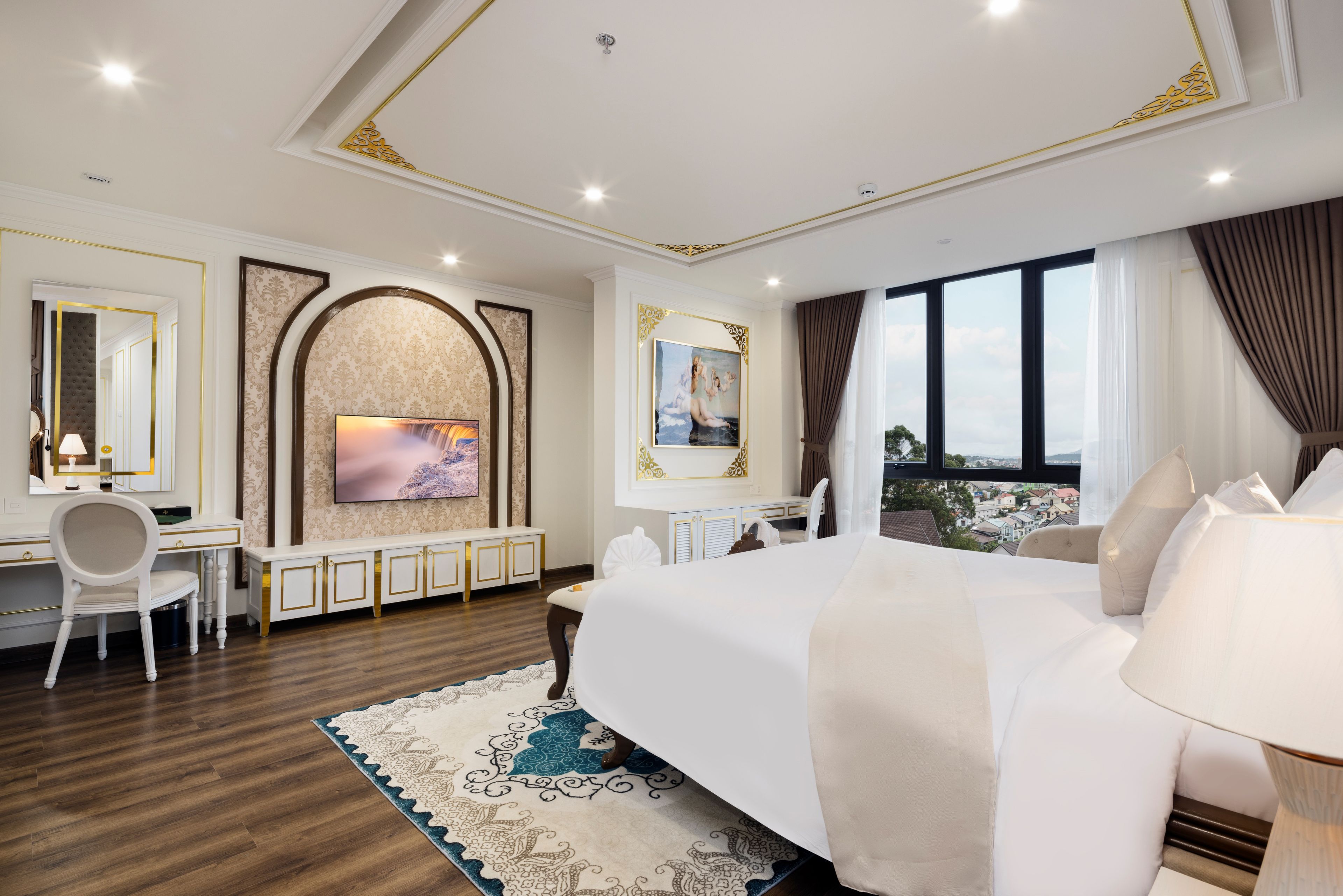 Habitación de hotel con una cama grande, un escritorio, una silla, un televisor y vistas de la ciudad a través de la ventana.