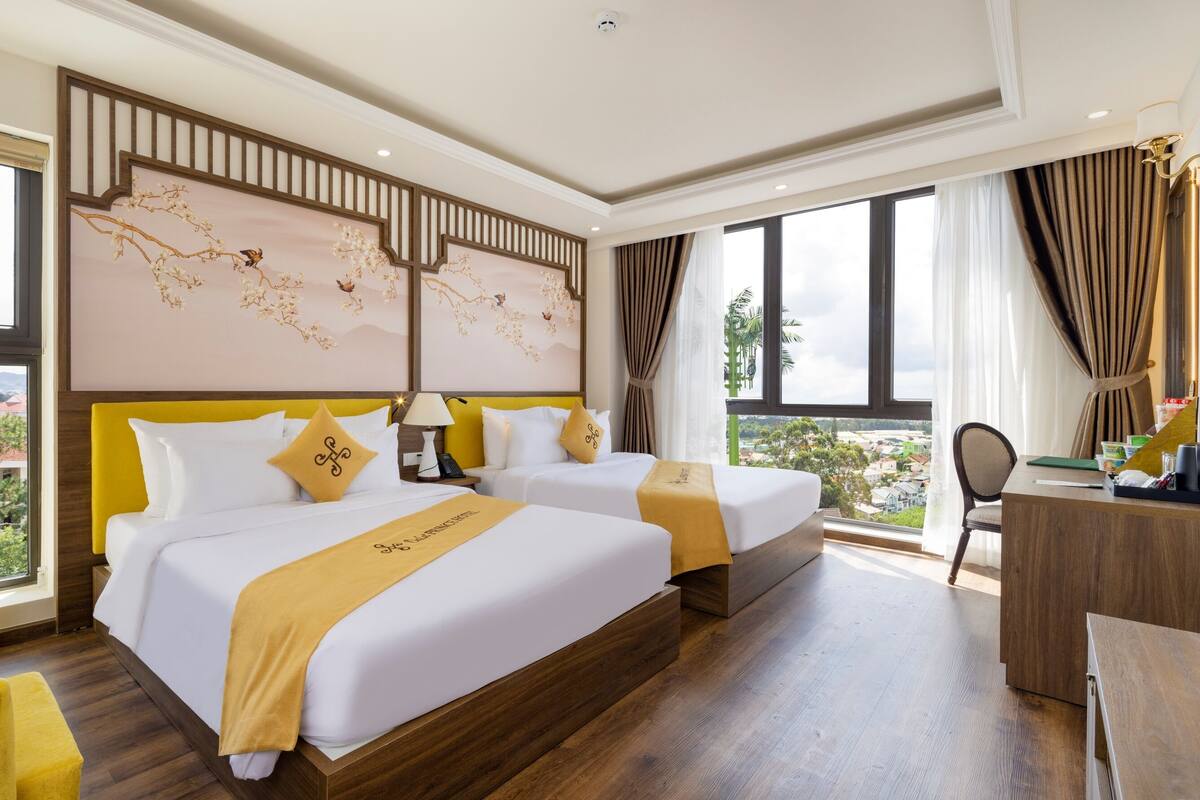 Ein Hotelzimmer mit zwei Betten, einem Schreibtisch und Blick auf die Stadt.