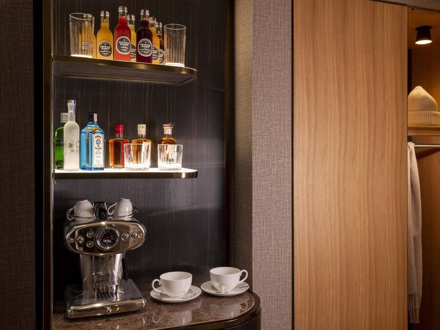 Zona de bar con una máquina de café, dos tazas y una estantería con varias botellas.