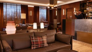 A modern hotel lobby with a leather sofa, a bar area, and wooden paneling. - Villa-des-Prés (Paris)