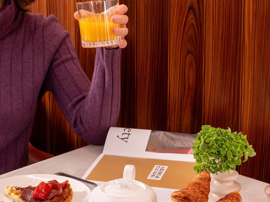 A breakfast setting with a table set for two, including croissants, a teapot, a cup of tea, and a glass of orange juice.