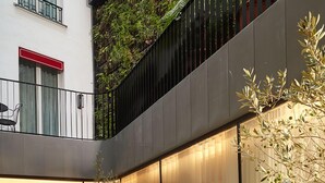 A modern outdoor seating area with multiple tables and chairs, surrounded by potted plants and a glass wall. - Villa-des-Prés (Paris)